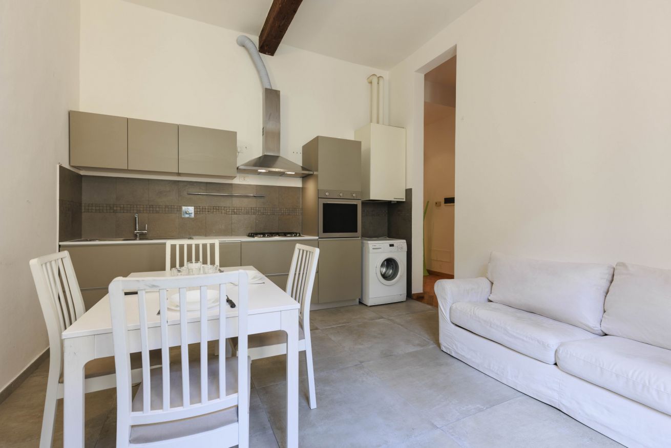 Een kleine keuken met een eettafel en stoelen, een wasmachine en een bank.
