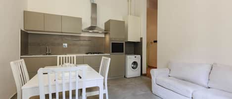 Cocina compacta con una mesa de comedor y sillas, lavadora y sofá.