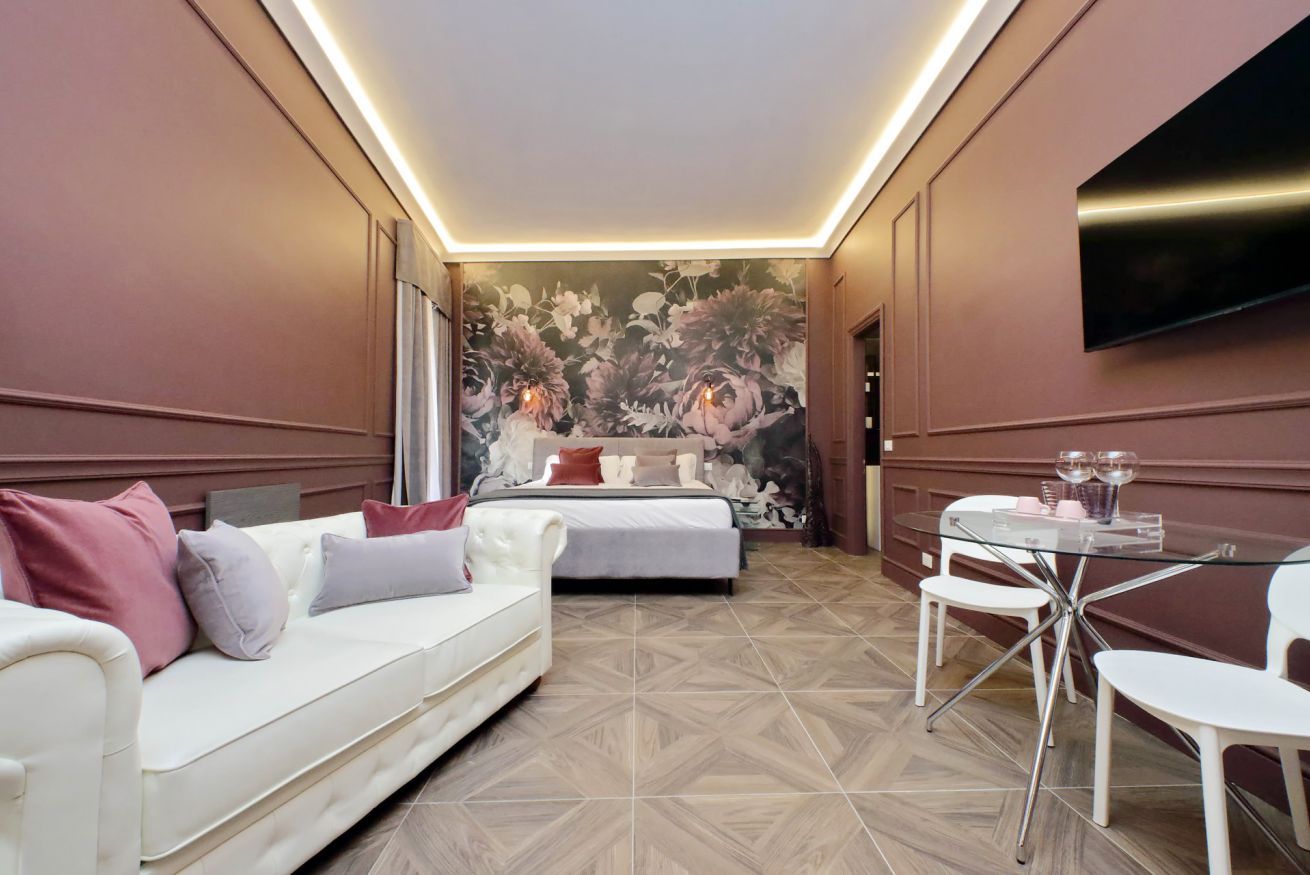 A modern hotel room with a bed, a white sofa, a glass dining table, and a large floral mural on the wall.