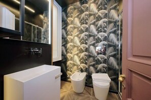 A modern bathroom with a large white bathtub, a bidet, and a toilet. The walls have a tropical leaf pattern wallpaper. - Suite Butterfly -Porpora (Roma)