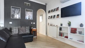 A modern living room with a black leather sofa, a flat-screen TV mounted on the wall, and a bookshelf filled with books and decorative items. - Florence Central Market (Firenze)