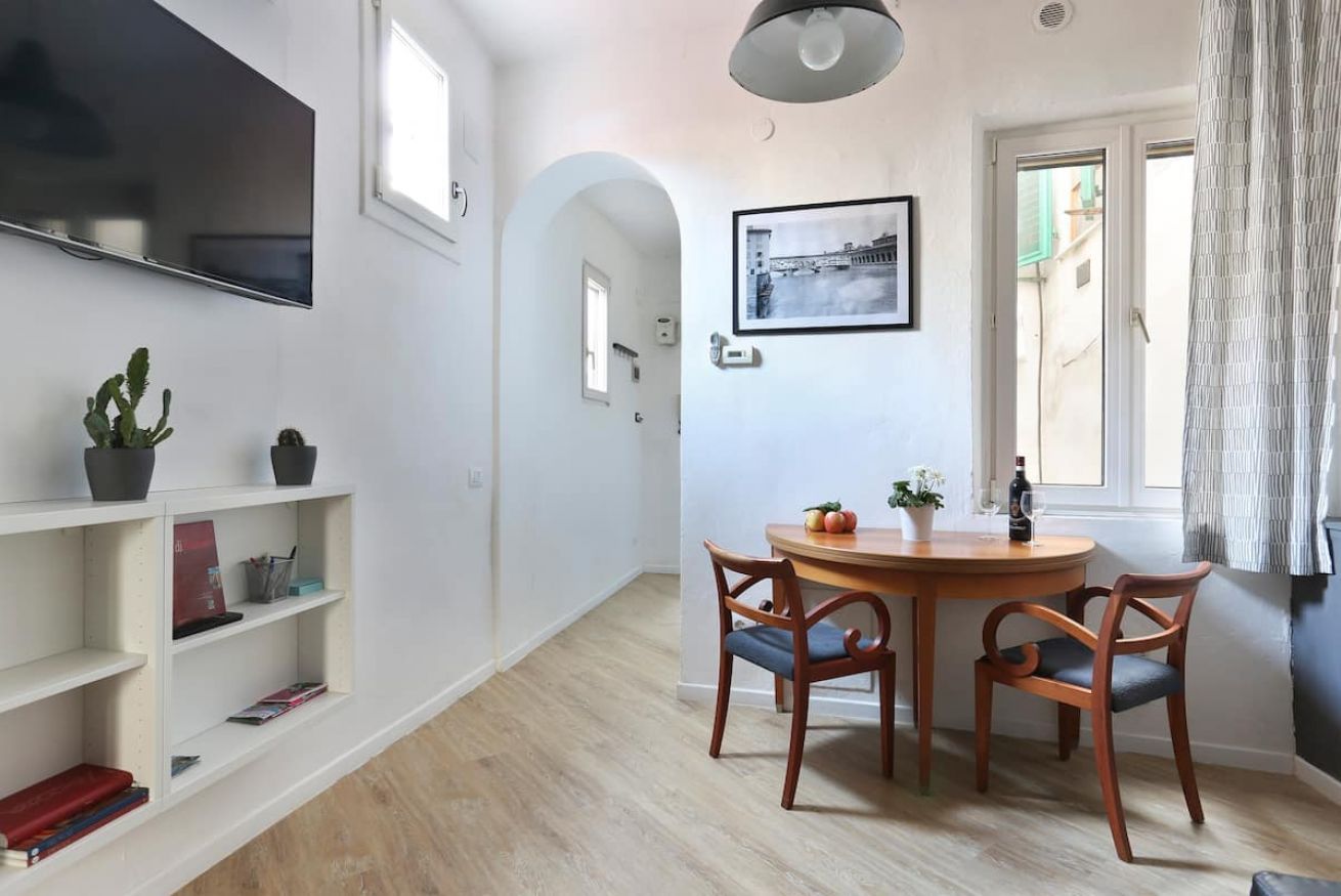 A dining area with a round wooden table, two chairs, a potted plant, and a framed picture on the wall.
