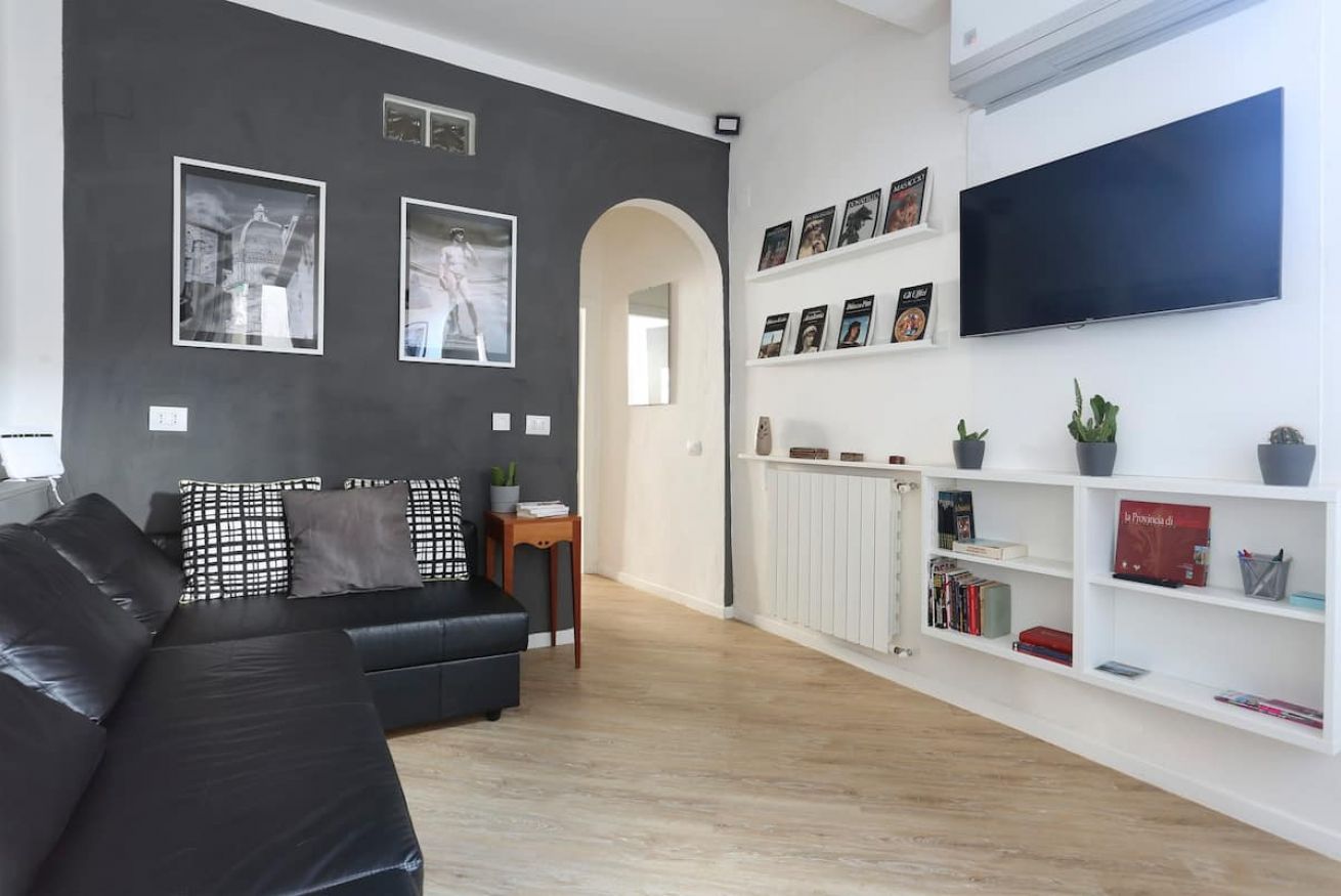 Een moderne woonkamer met een zwarte leren bank, een flatscreen televisie aan de muur en een boekenplank vol boeken en decoratieve objecten.