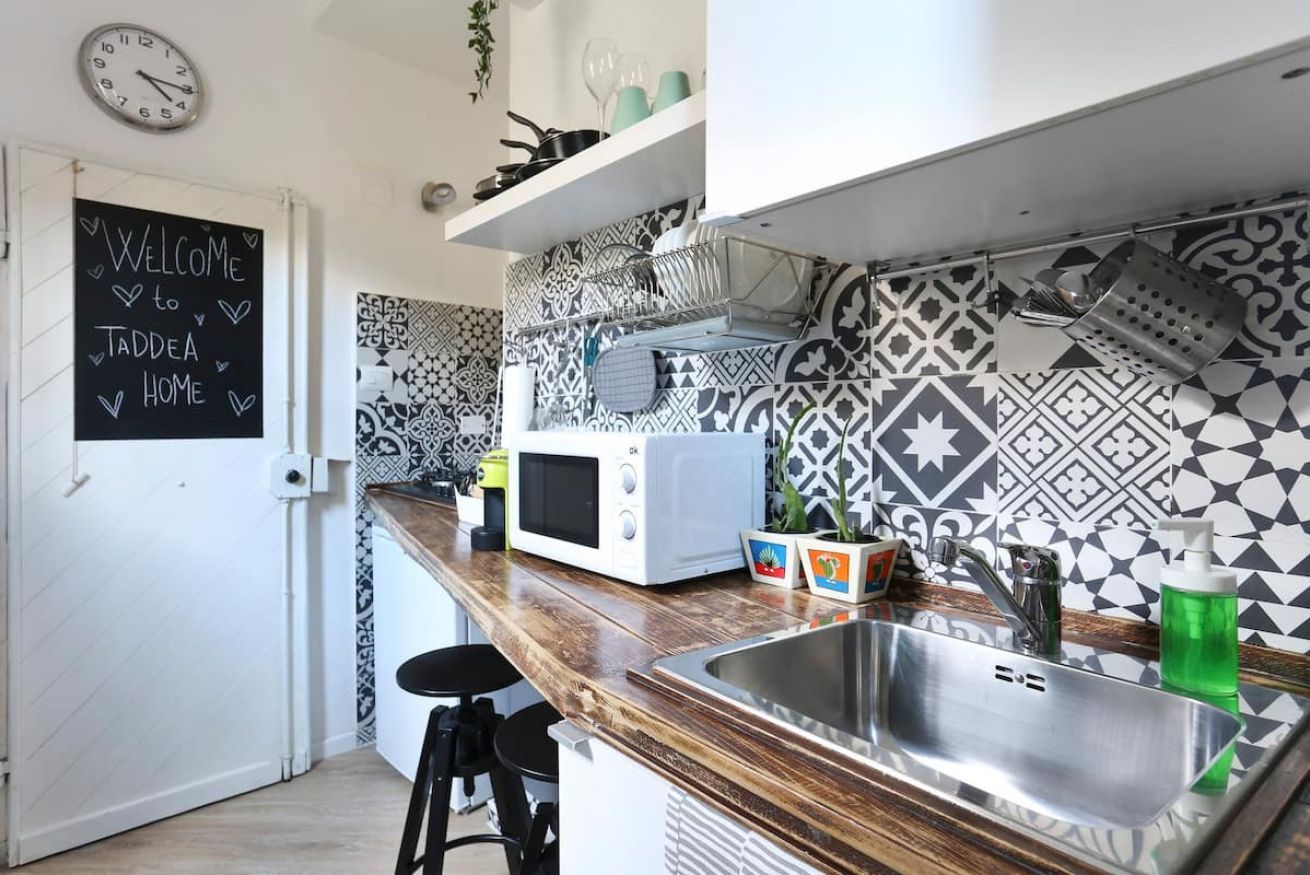 A kitchen with a chalkboard sign, patterned tiles, a microwave, a sink, and bar stools.