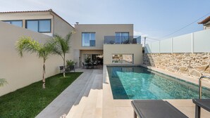 Ein modernes Haus mit Swimmingpool, einer Terrasse und Gartenmöbeln sowie einer Steinmauer.