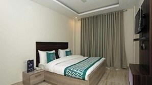 A modern hotel room with a wooden bed, a nightstand, a TV, and a large window with curtains. - Hotel Lakshmi Palace (New Delhi)