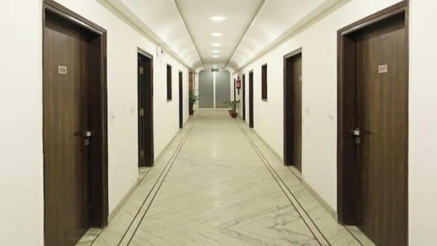 A long, narrow hallway with doors on both sides, leading to individual rooms. - Hotel Lakshmi Palace (New Delhi)