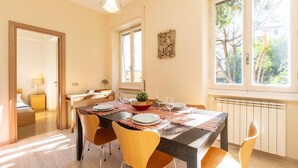 A dining area with a table set for four, a window with a view of trees, and a radiator under the window. - Rental in Rome Pateras Garden Apartment (Rome)