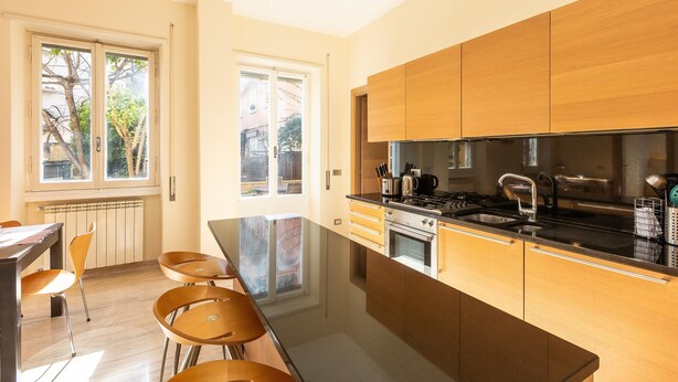 A modern kitchen with wooden cabinets, a large island, and a view of the outside. - Rental in Rome Pateras Garden Apartment (Rome)
