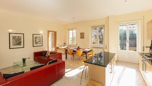 A modern living room with a red sofa, glass coffee table, and dining area with yellow chairs. - Rental in Rome Pateras Garden Apartment (Rome)