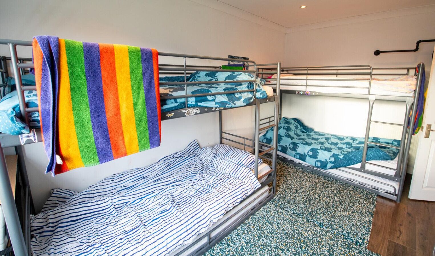 Une chambre avec un lit superposé, une serviette aux couleurs de l’arc-en-ciel, une literie à rayures et un tapis à motifs.