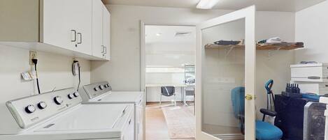 A laundry area with a washing machine, a dryer, and a small desk with a chair.