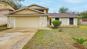 A single-story house with a stone facade, a beige garage door, and a small front yard with a young tree and a well-maintained lawn. - Near Six Flags & Seaworld: San Antonio Family Home (San Antonio)