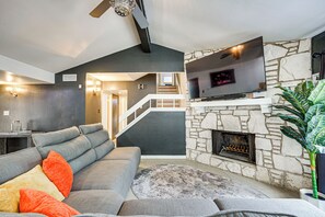 En moderne stue med en grå hjørnesofa, en stenspir, et fladskærms-tv og en trappe til en etage over.