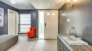 A modern living room with a grey sofa, a red chair, a glass coffee table, and a door leading to another room. - Near Six Flags & Seaworld: San Antonio Family Home (San Antonio)