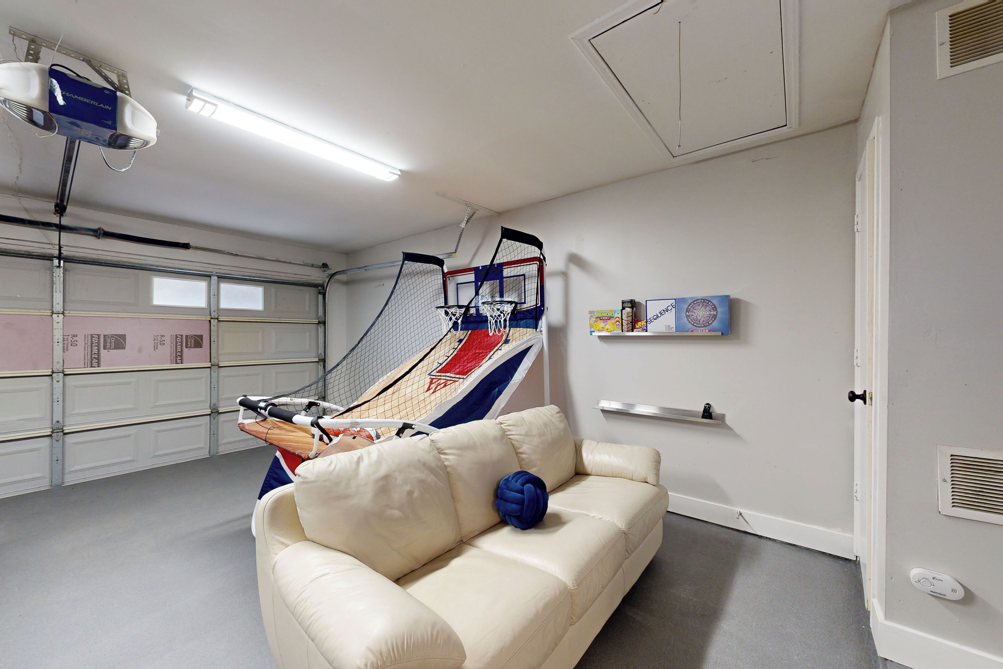 A room with a white leather couch, a basketball hoop, and a ceiling-mounted projector.