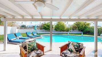 A covered outdoor area with a pool, lounge chairs, and a table.