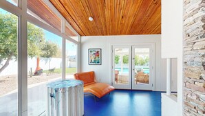 A room with a wooden ceiling, large windows, a blue floor, a stone wall, and a door leading outside. - 3BR Home w/ Game Room, Heated Pool & Large Yard (Scottsdale)