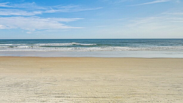 A beach with a clear sky and calm sea. - Steps to Ocean: Daytona Beach Condo w/ Patio! (Daytona Beach)