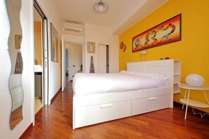 Ein Schlafzimmer mit einem weißen Bett, Holzboden, einer gelben Wand und einem Gemälde.