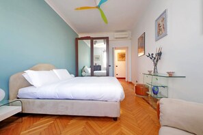 A bedroom with a bed, a glass side table, a chair, a ceiling fan, and a door leading to another room. - UNA FINESTRA SULLA CUPOLA DI SAN PIETRO (Roma)
