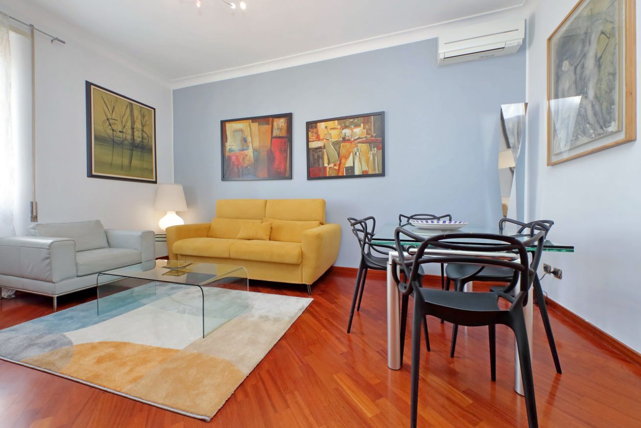 A modern living room with a sofa, a dining table with chairs, and artwork on the walls.