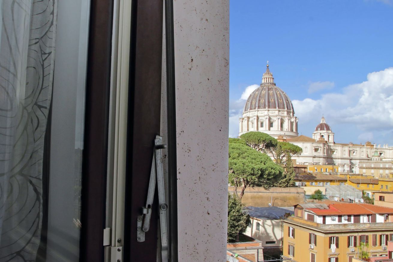 A view of a historic building with a large dome and classical architecture, seen through a window with a curtain.