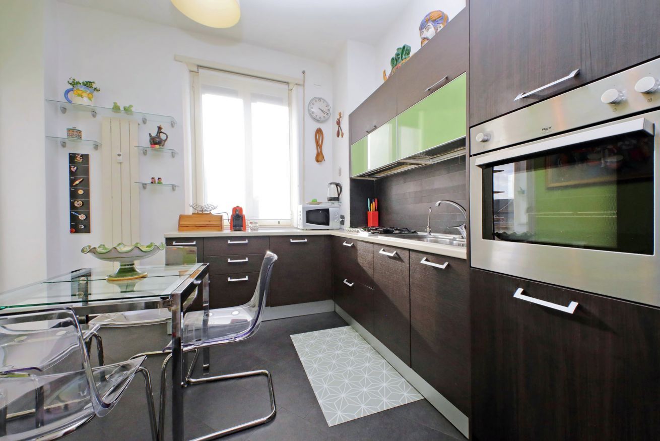 A modern kitchen with dark wooden cabinets, stainless steel appliances, and a glass dining table.