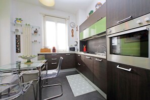 Cozinha moderna com armários de madeira escura, eletrodomésticos de aço inoxidável e uma mesa de jantar de vidro.