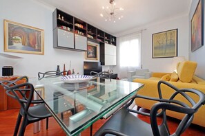Ein modernes Wohnzimmer mit einem Glastisch, schwarzen Stühlen, einem gelben Sofa und einem Bücherregal.
