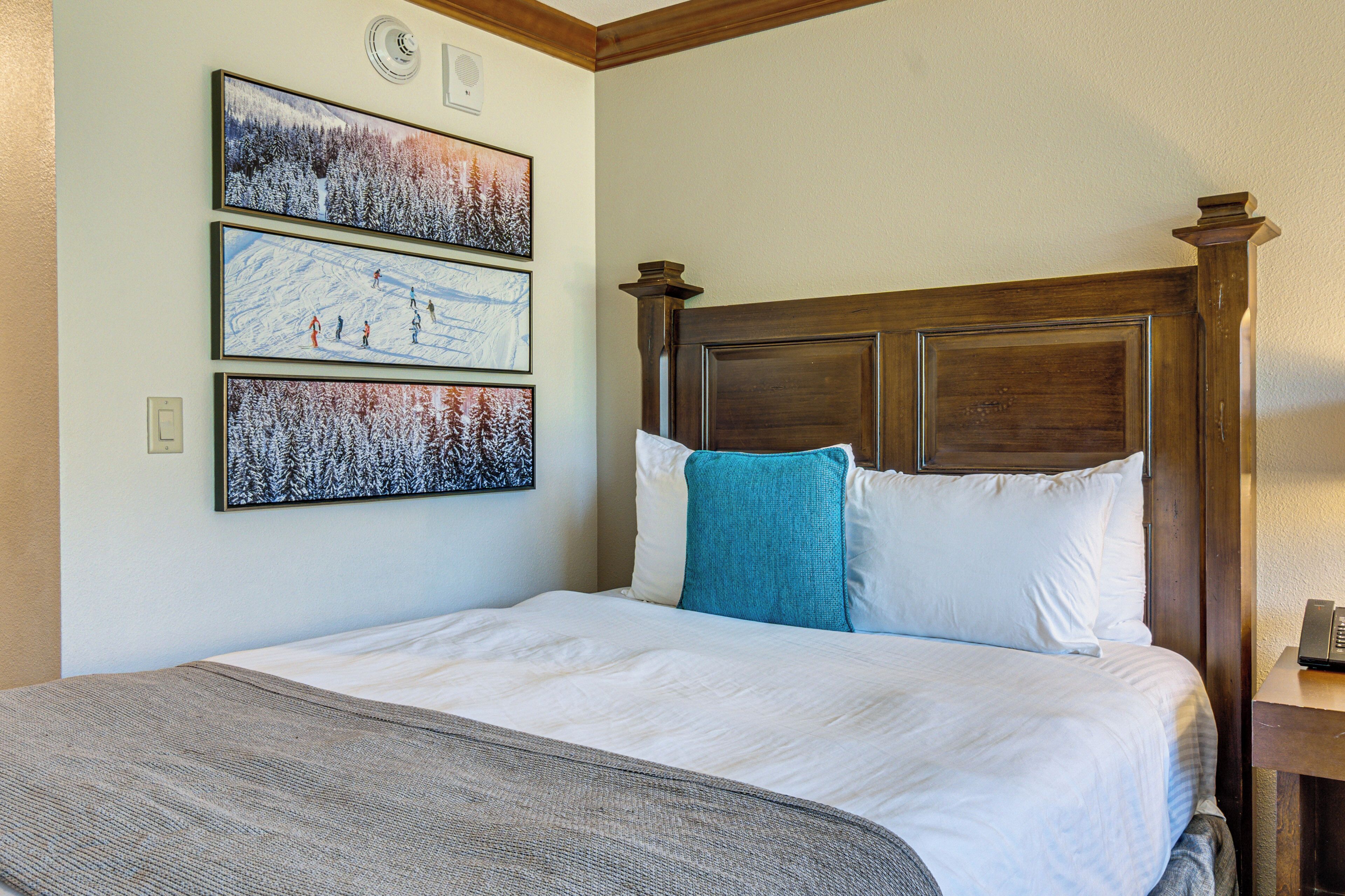 A neatly made bed with a wooden headboard, a gray throw blanket, and three framed pictures on the wall.