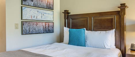 A neatly made bed with a wooden headboard, a gray throw blanket, and three framed pictures on the wall.