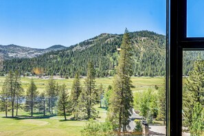 A view through a window of a mountainous landscape with a golf course, trees, and a clear sky. - Hike, Ski & Ice Skate! Everline Resort Studio (Olympic Valley)