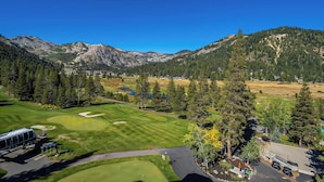 A golf course with a mountain backdrop, a parking area, and a building with a flag. - Olympic Valley Studio For Summer: Everline Resort! (Olympic Valley)