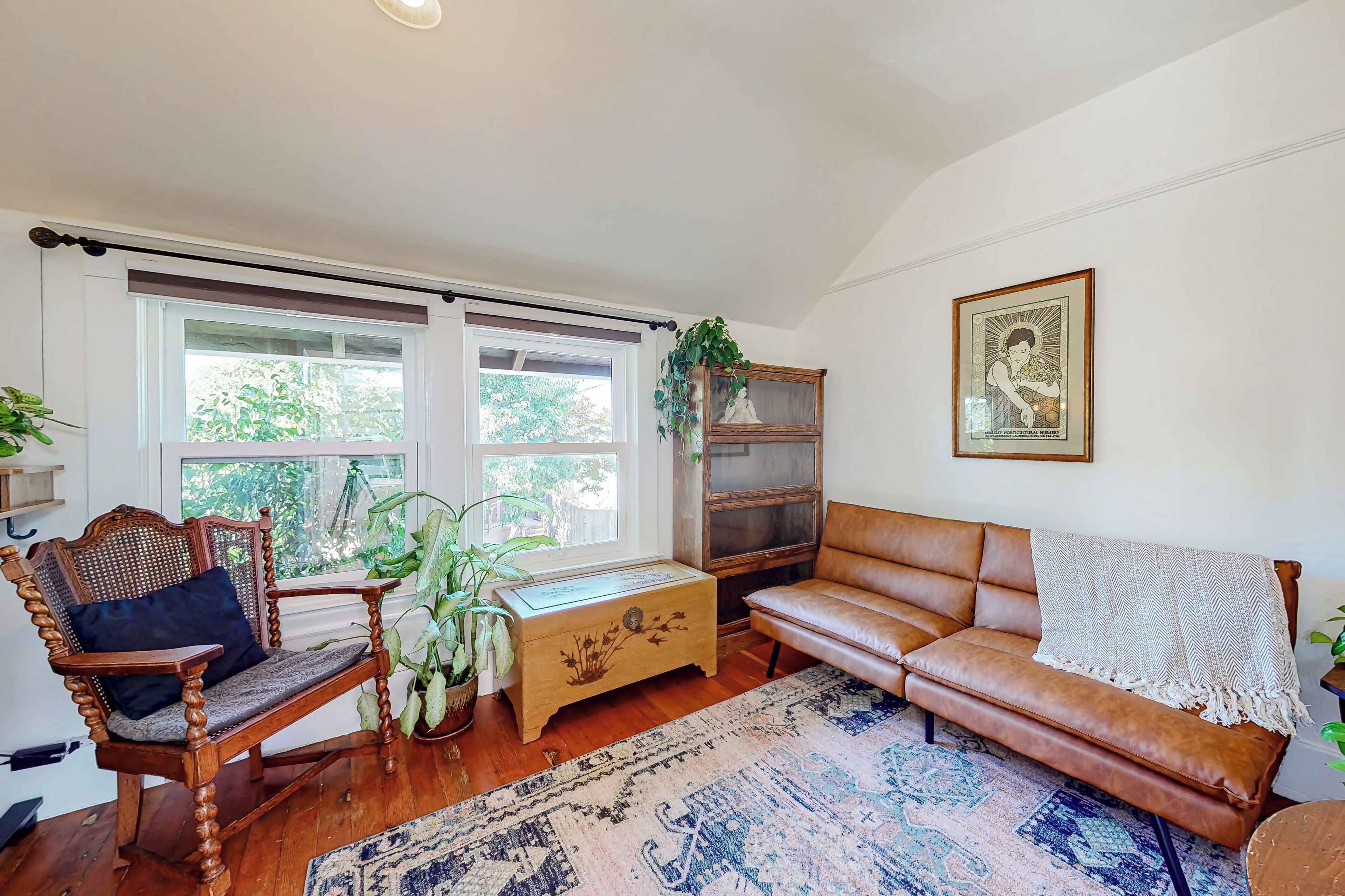 A cozy living room with a wooden sofa, a wooden bench, a wooden chest of drawers, and a large window with a view of greenery outside.