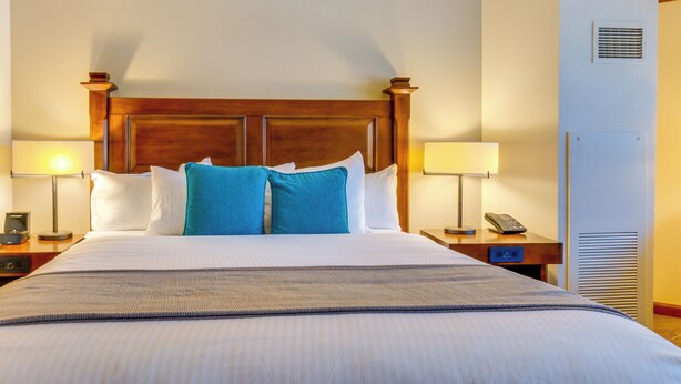 Una camera d'albergo con un letto grande, due comodini con lampade, una testiera in legno e una bocchetta d'aria a parete.