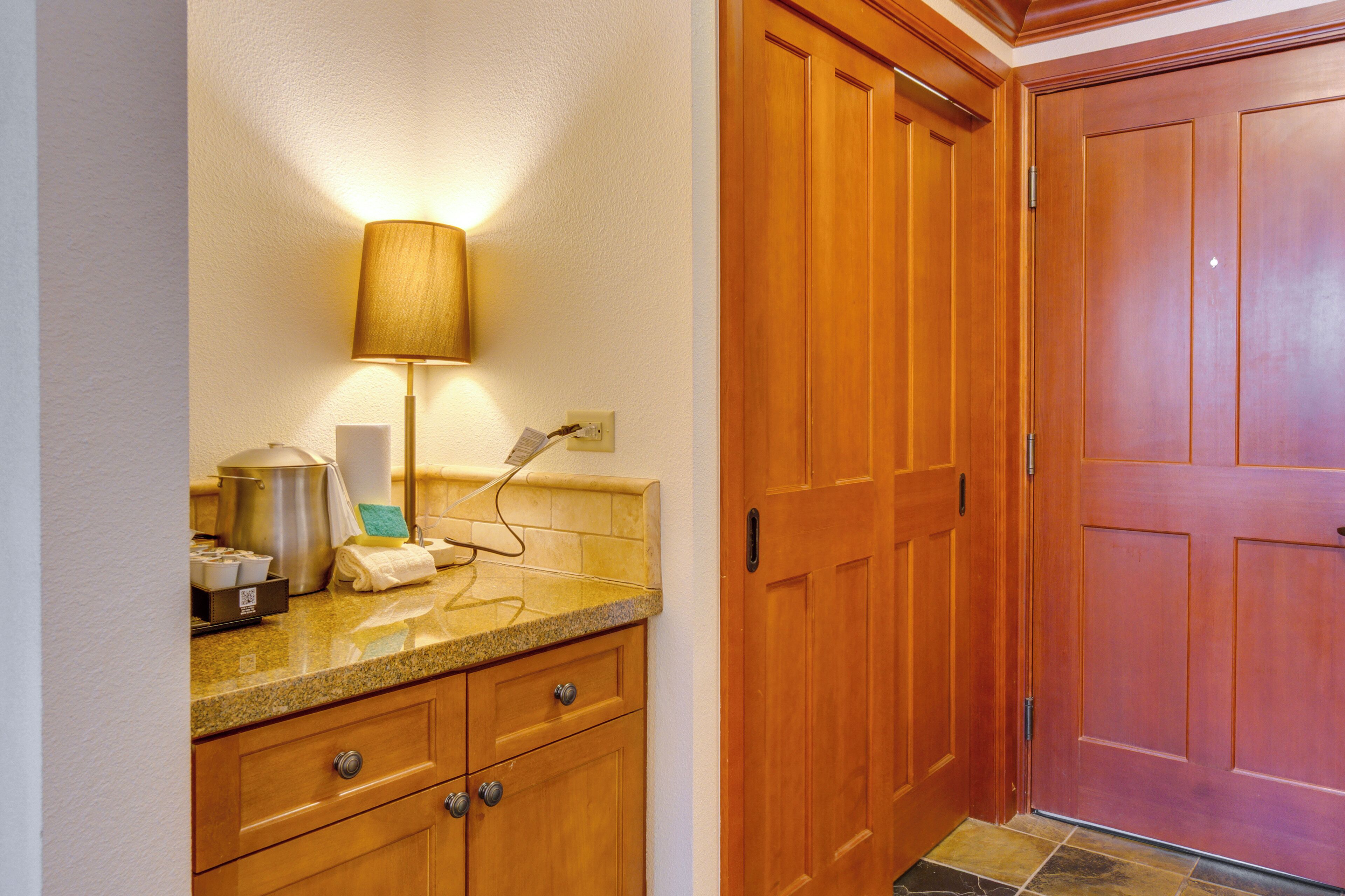 A kitchen with granite countertops, wooden cabinets, a stainless steel pot, and a lamp.