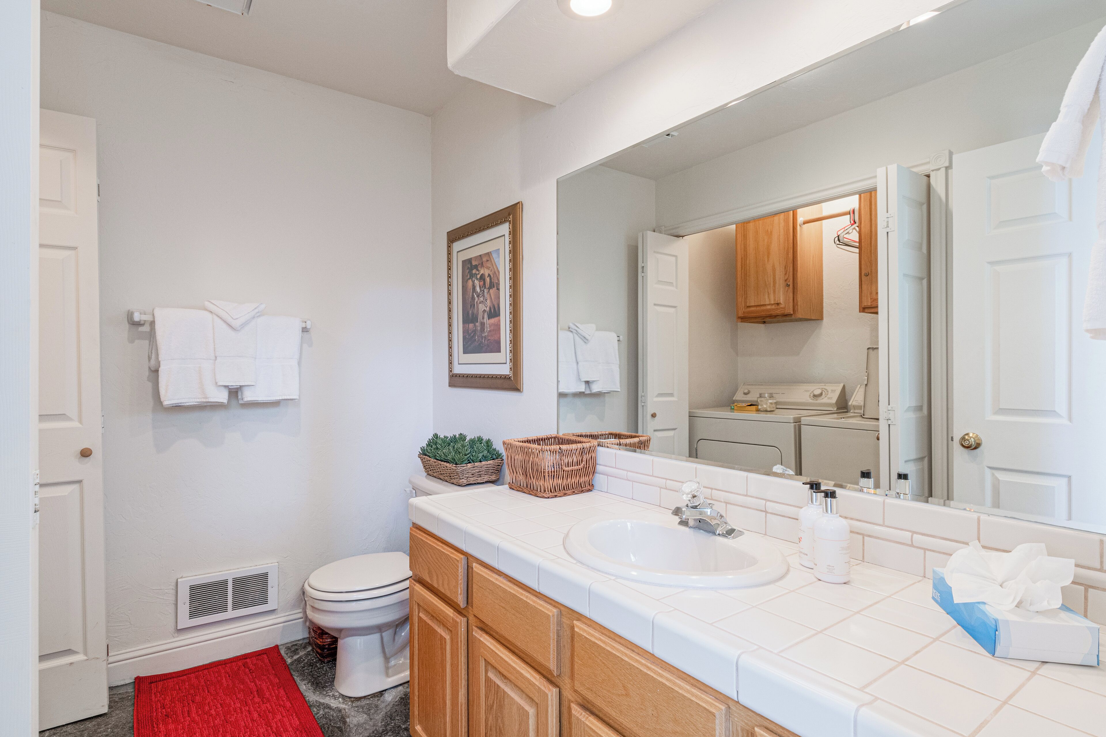 Un baño con un lavamanos blanco, armarios de madera, un tapete rojo y un espejo que refleja la habitación.