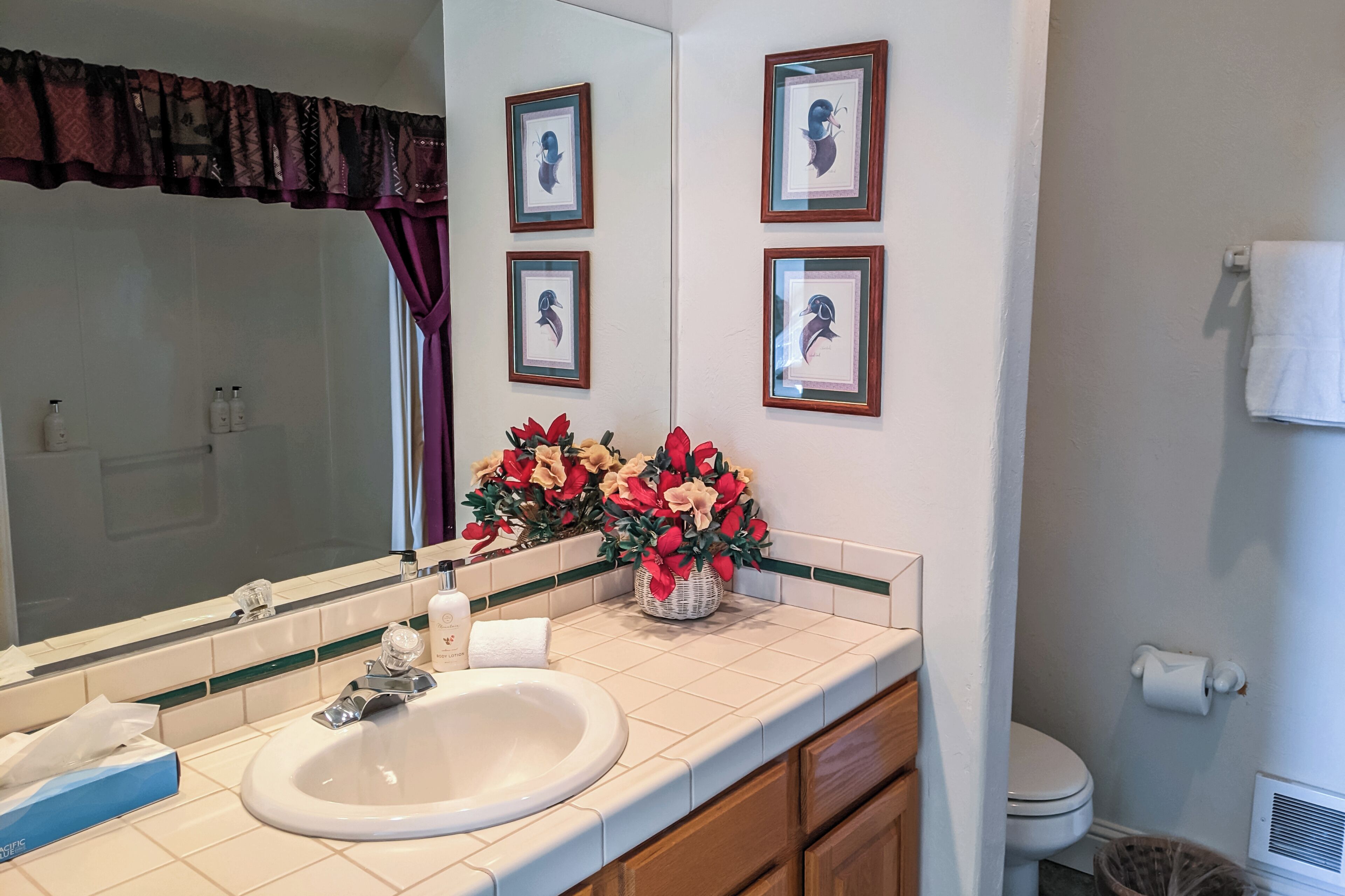 A bathroom with a sink, mirror, framed pictures, and a vase of flowers.