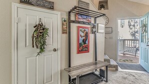 A hallway with a white door, a bench, and a poster of a movie. There are signs above the door and a small shelf with a plant. - Walk to Midtown Ruidoso! Cozy Eagles Nest Condo (Ruidoso)