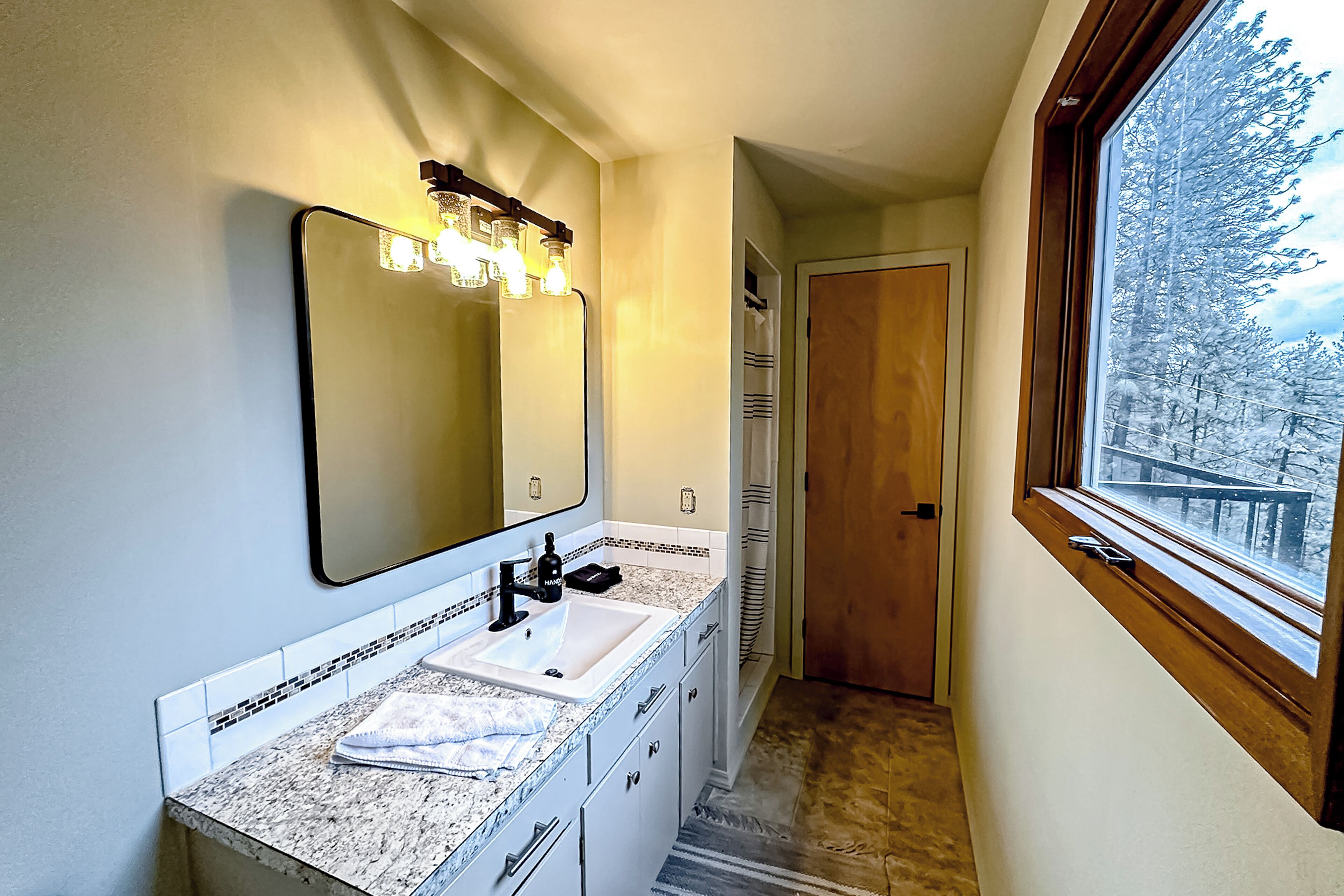 A bathroom with a large mirror, a sink, and a window.