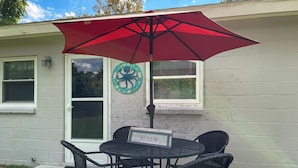 En terrasse med et bord og stole under en rød parasol, et skilt med teksten "BEACH" og et velkomstskilt med et blæksprutte-design.