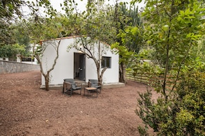 Un piccolo edificio bianco con una porta, due sedie e un tavolo in un giardino.