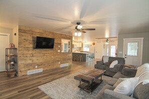 A spacious living room with a wooden accent wall, a ceiling fan, and a large flat-screen TV mounted on the wall. - Fish Hatchery Ranch w/ Furnished Patio (Hatch)