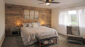 Une chambre à coucher avec une tête de lit en bois, un lit avec des oreillers, un banc, une chaise et un ventilateur de plafond.
