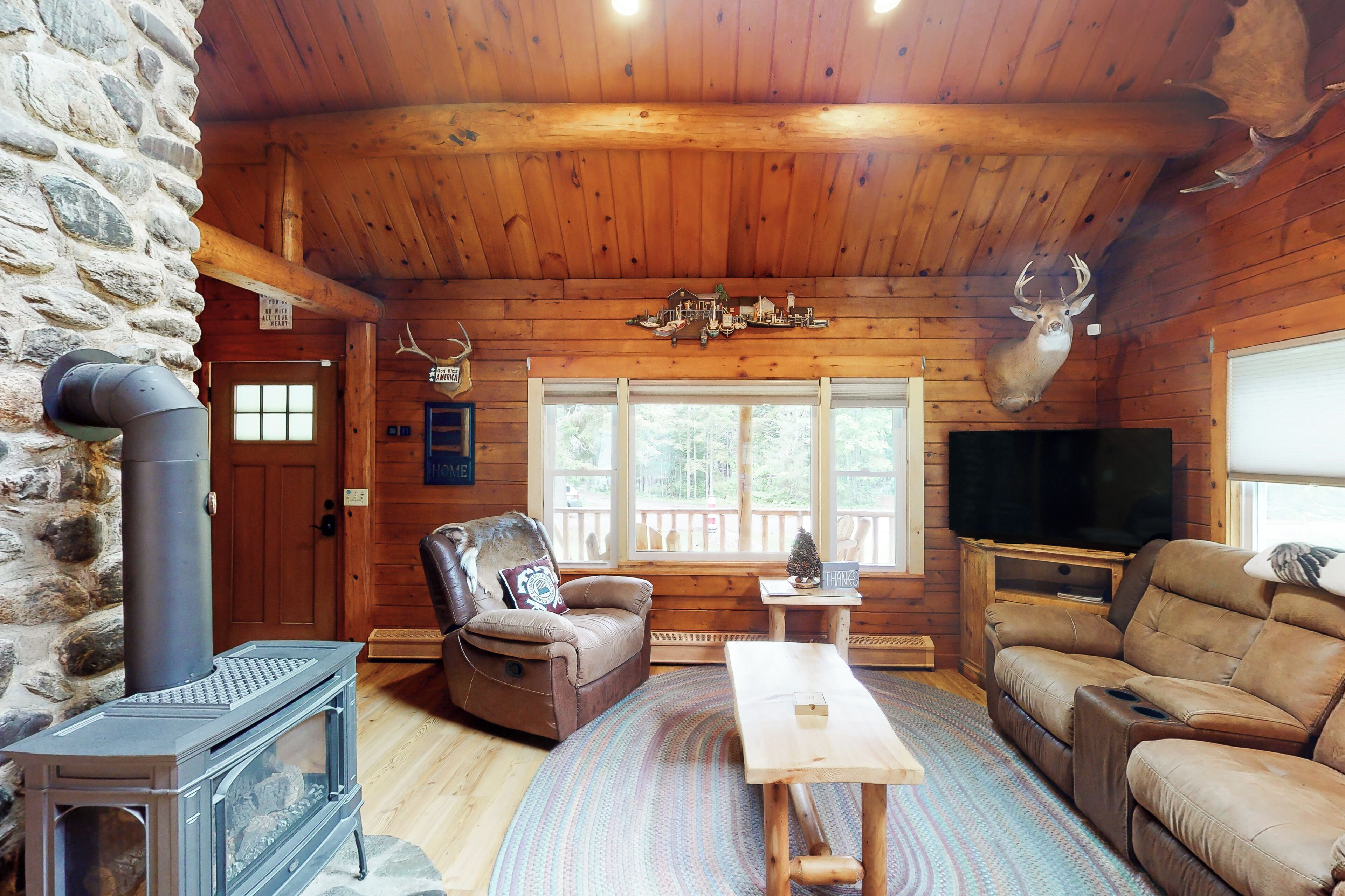 L’intérieur d’une cabane en rondins, avec un mur en pierre, un plafond en bois, une cheminée, un téléviseur et un coin salon confortable.