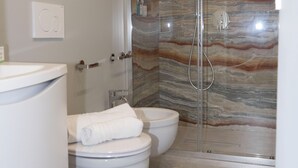 Een moderne badkamer met een douchewand van marmer, een toilet en een bidet.