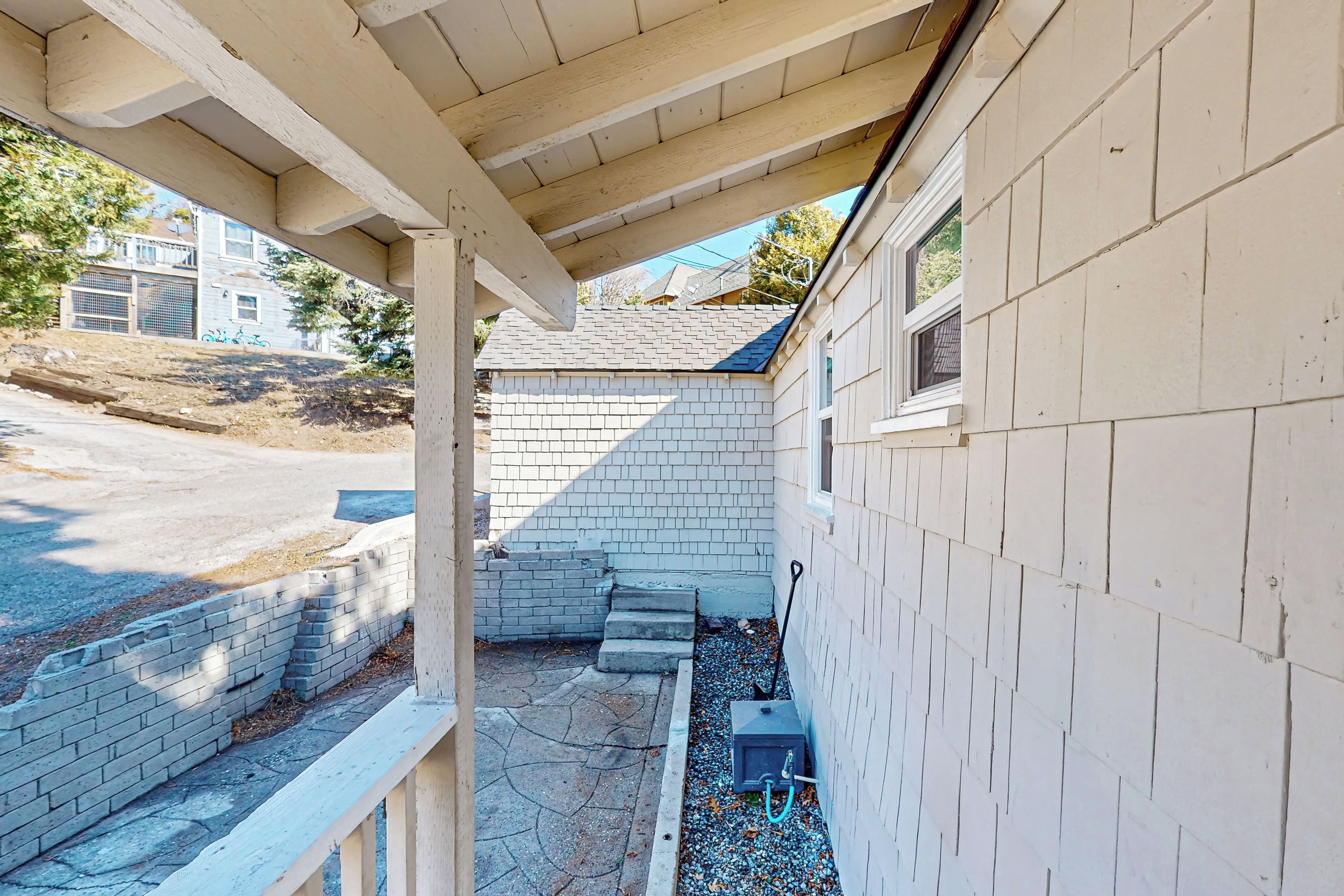 A covered outdoor area with a brick wall, steps leading to a driveway, and a utility box.