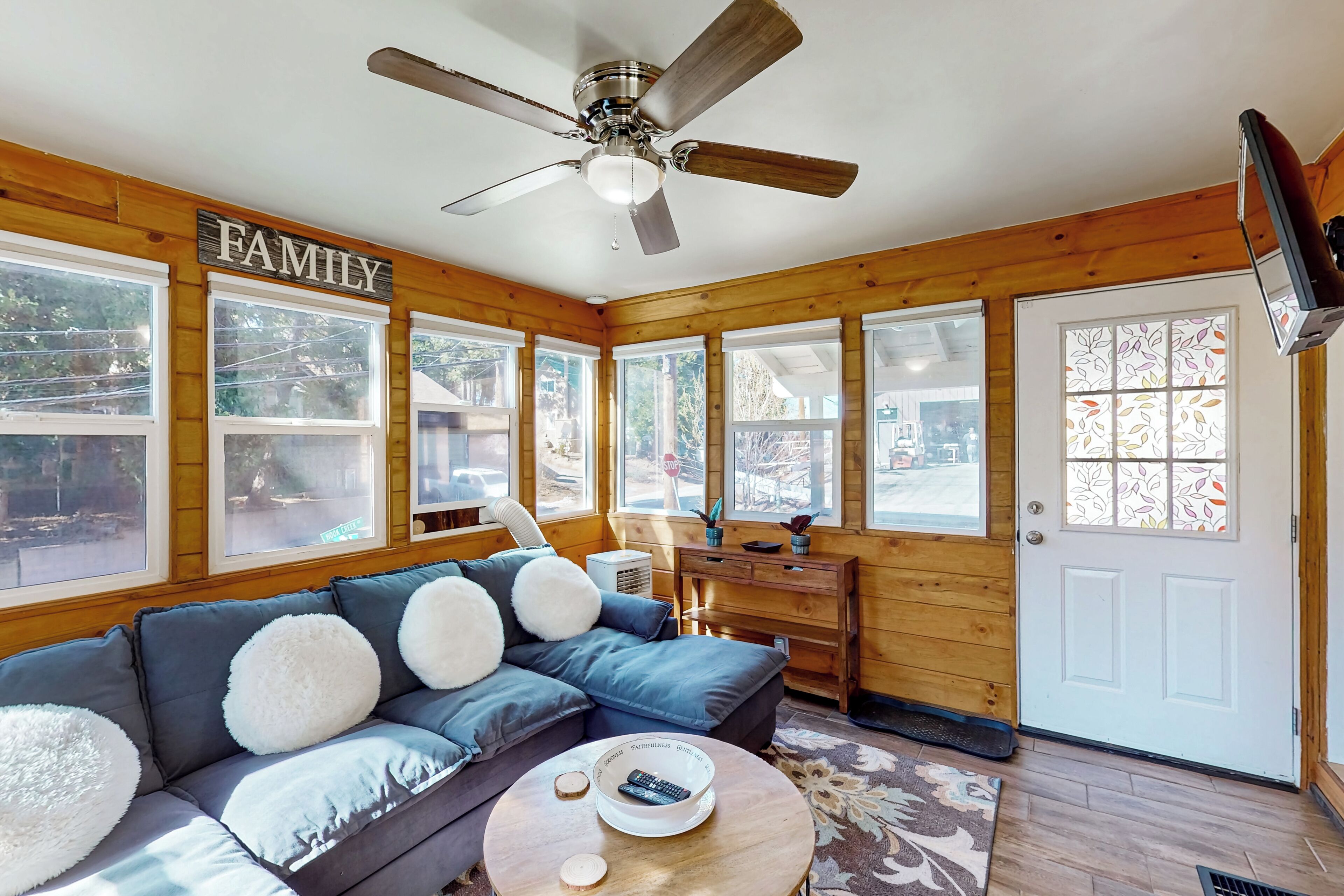 A cozy living room with a sectional sofa, a ceiling fan, and a 'FAMILY' sign on the wall.