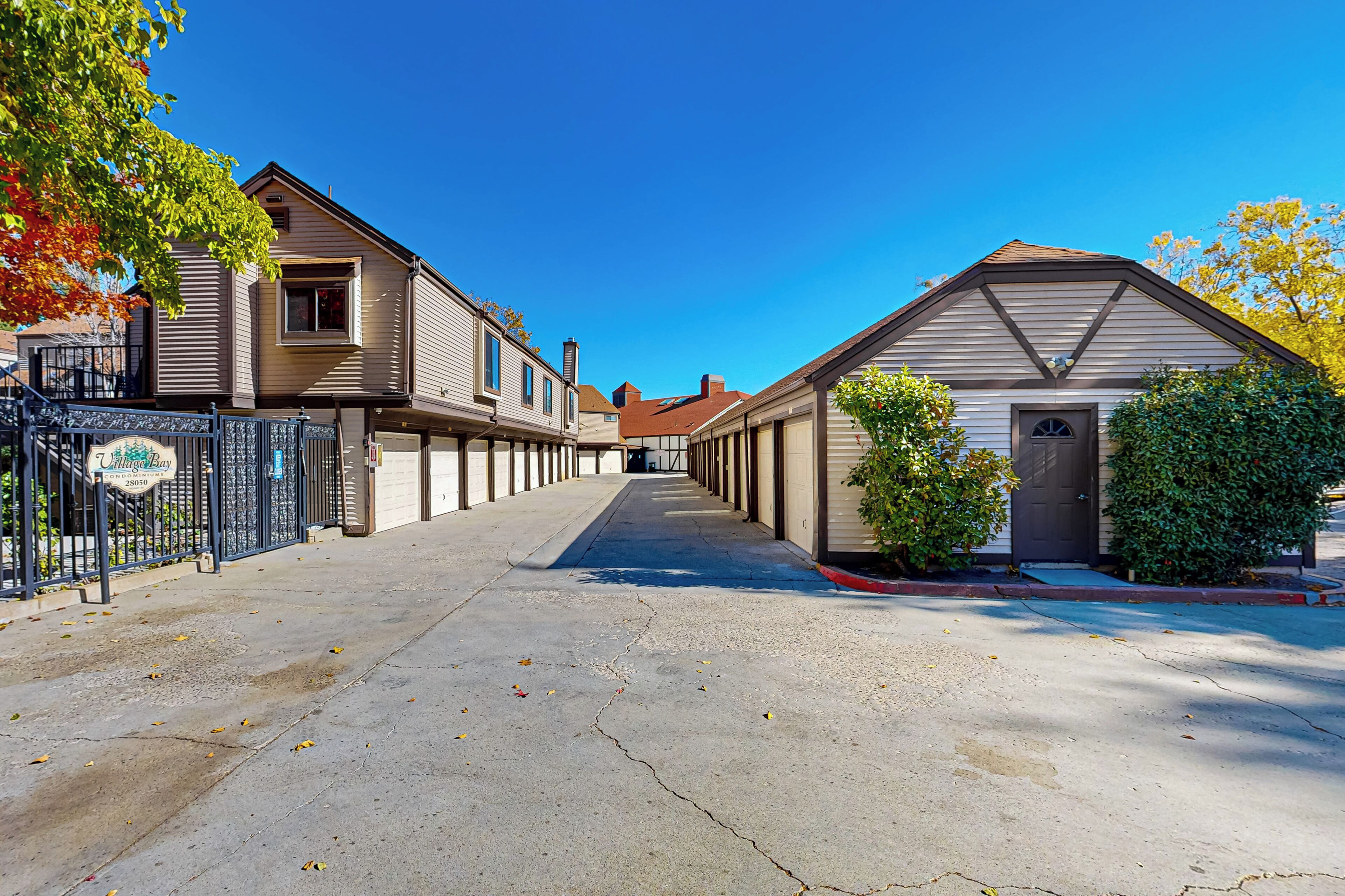 Une rue résidentielle bordée de maisons, avec une entrée sécurisée et un ciel dégagé.